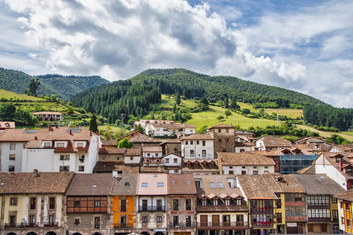 Quaint Spanish town with tiled rooftops and lush green hills behind.