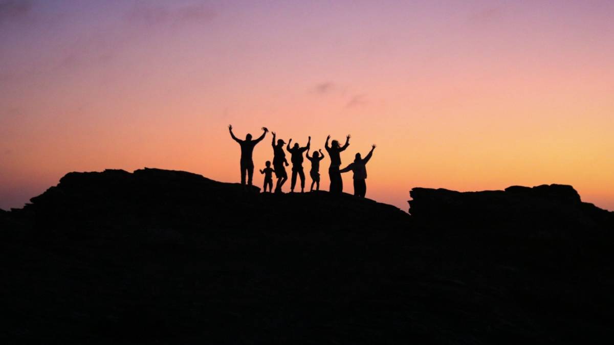 Silhouettes of people with arms raised against a sunset.
