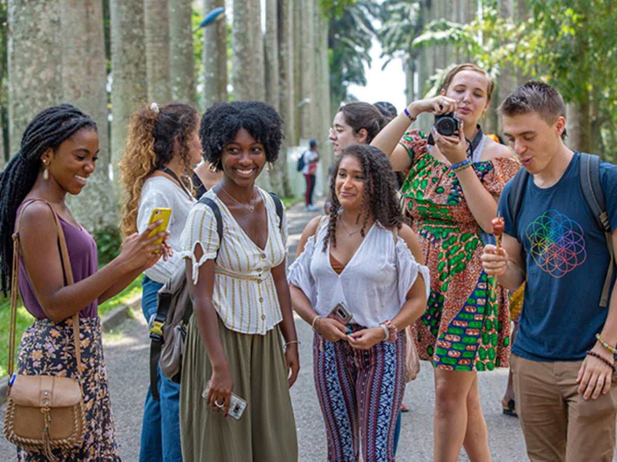 Smiling students stand outside among tall trees