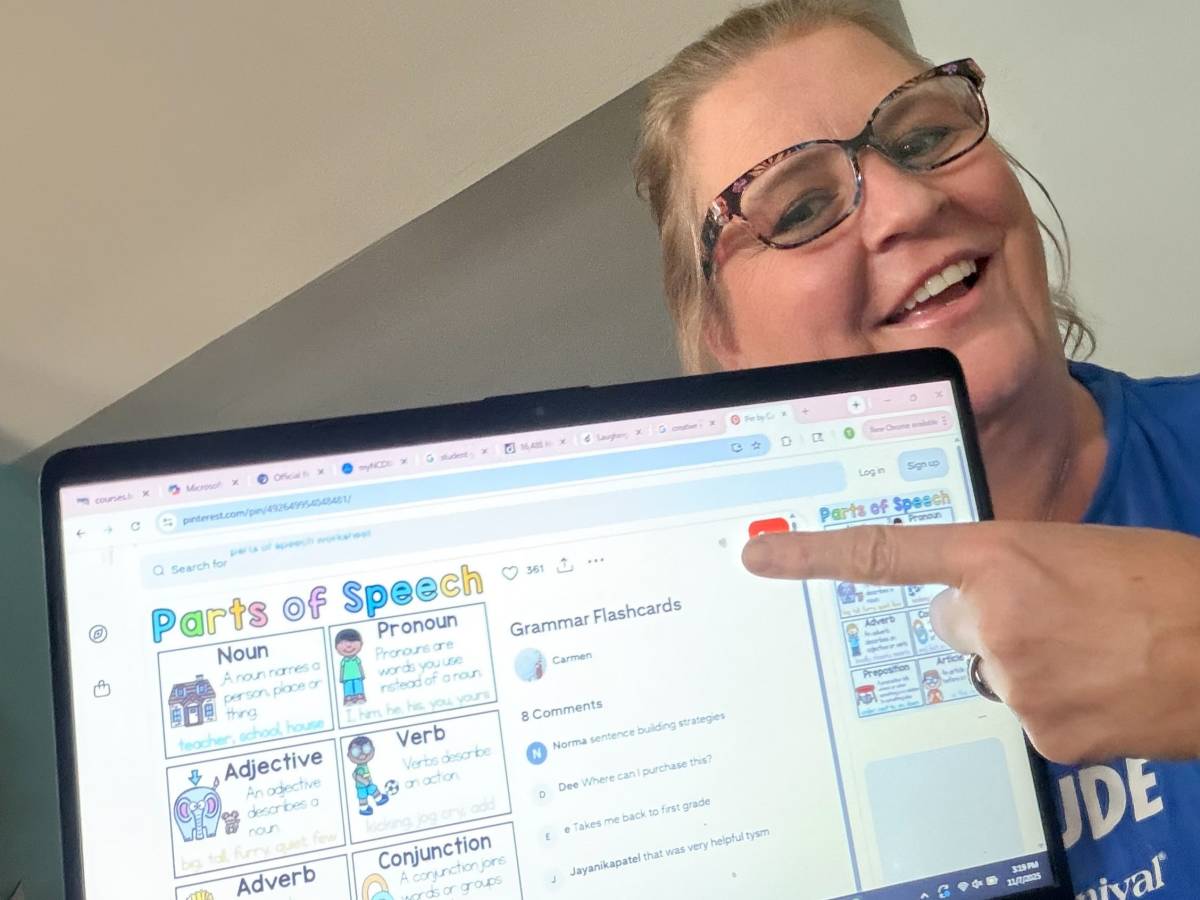 Smiling woman pointing to laptop screen, which shows teaching resources.