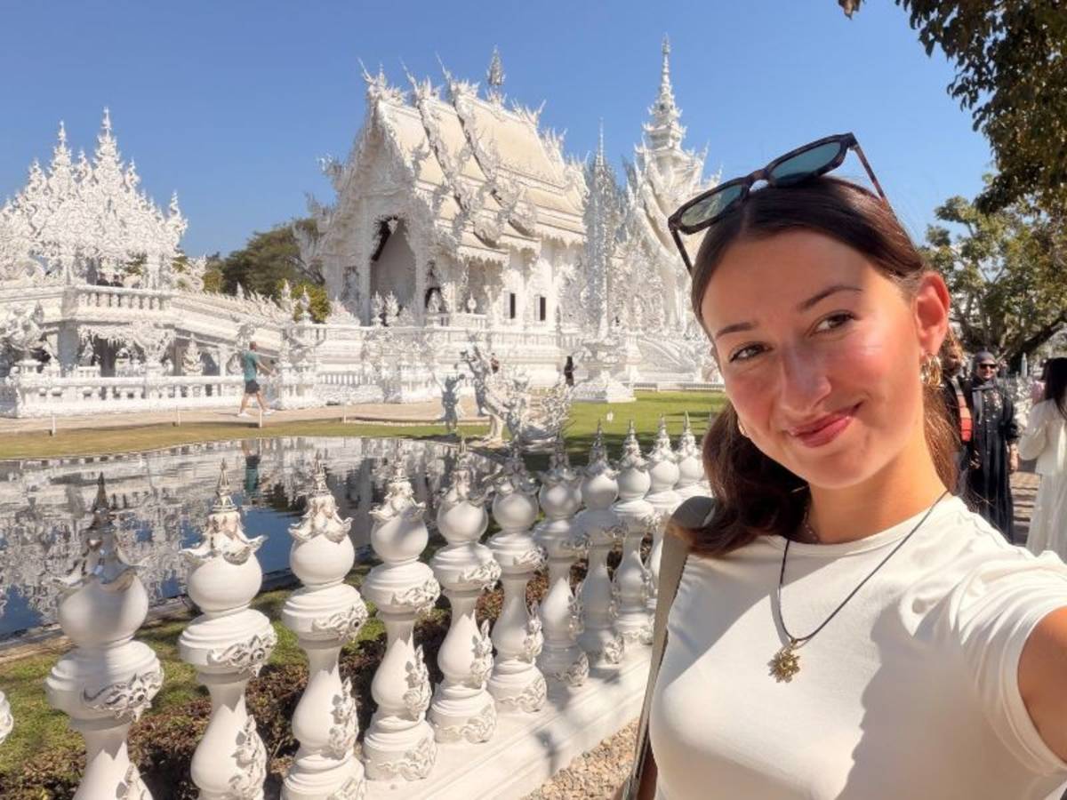 Smiling young woman taking a selfie in front of White Temple, in Chiang Rai, Thailand.