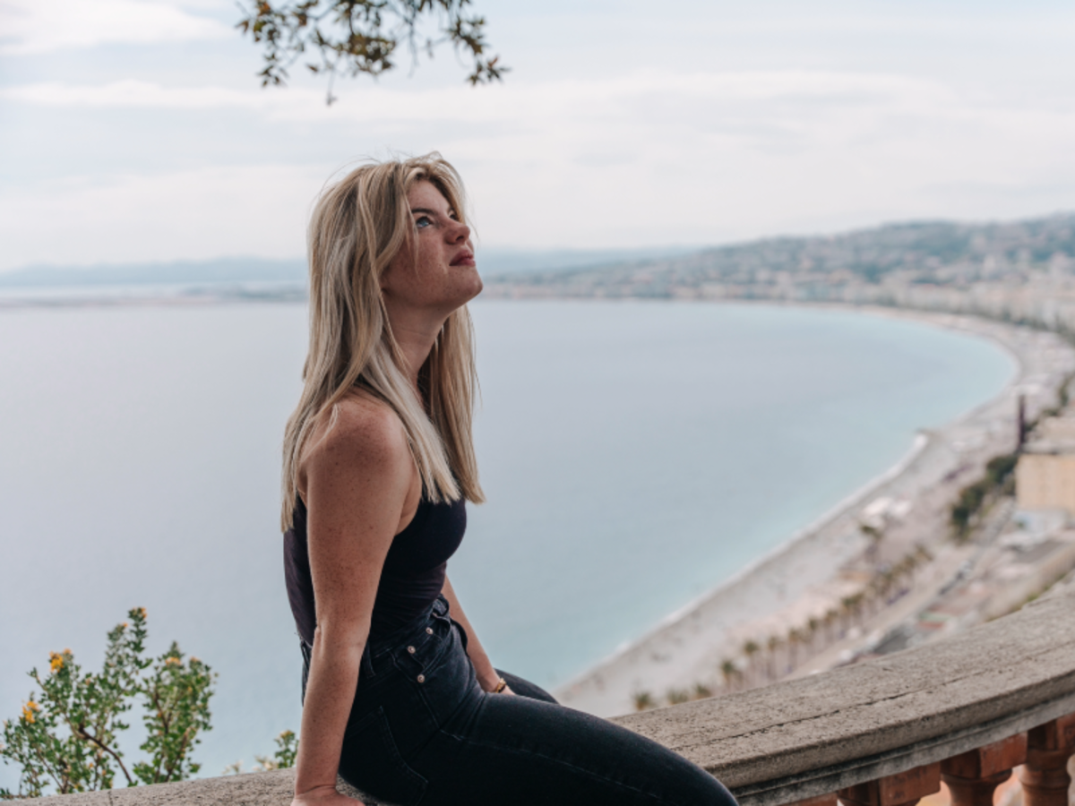 Student sitting on a ledge overlooking the Bay of Angels in Nice, with panoramic views of the coastline and Mediterranean Sea.