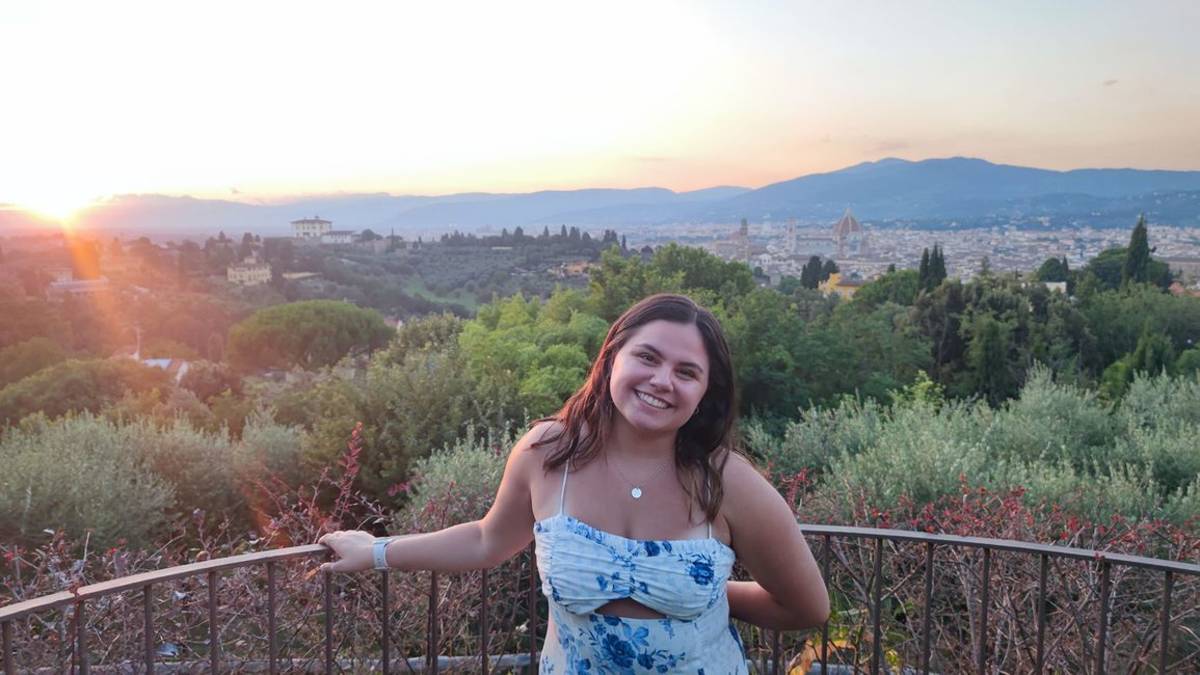 Student smiling with Italy skyline at sunset behind her