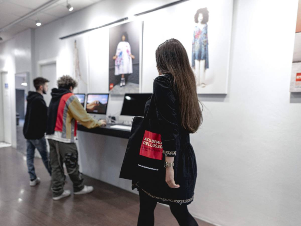 Student walking down a corridor with art on the walls. Two other students are standing at computers