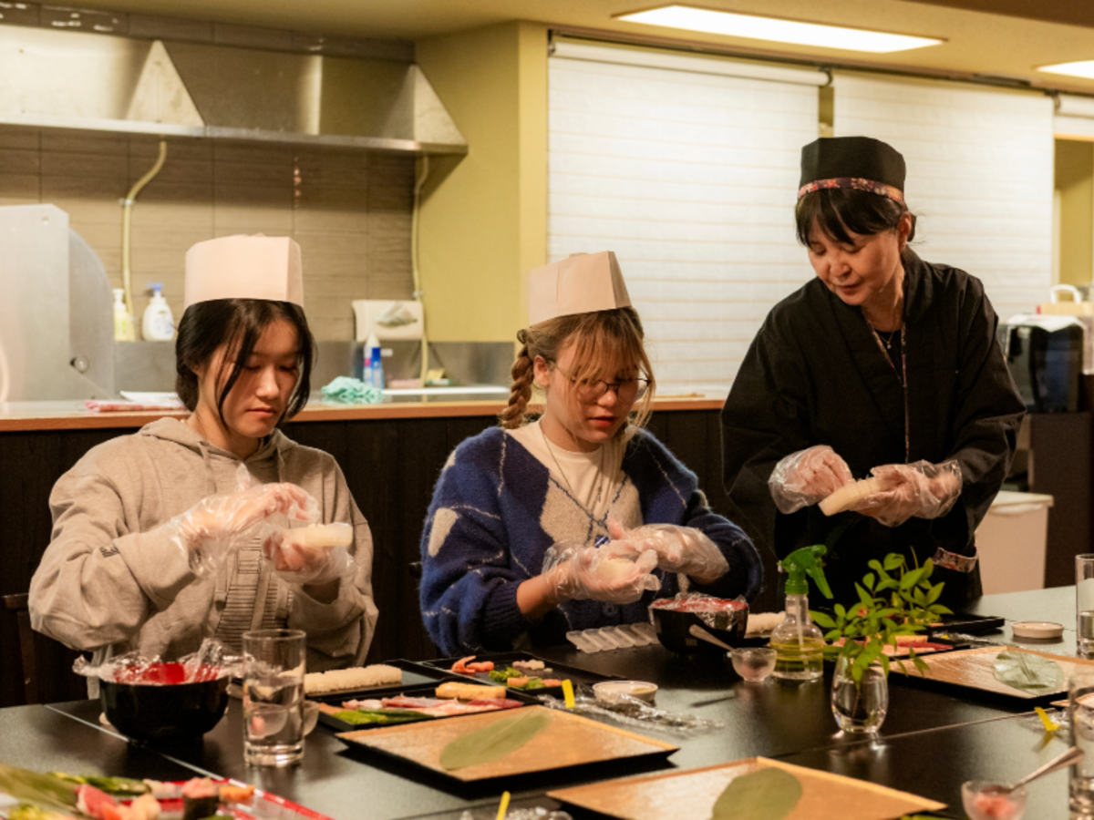 Students learning how to make sushi during a cooking class in Tokyo with guidance from a local chef.