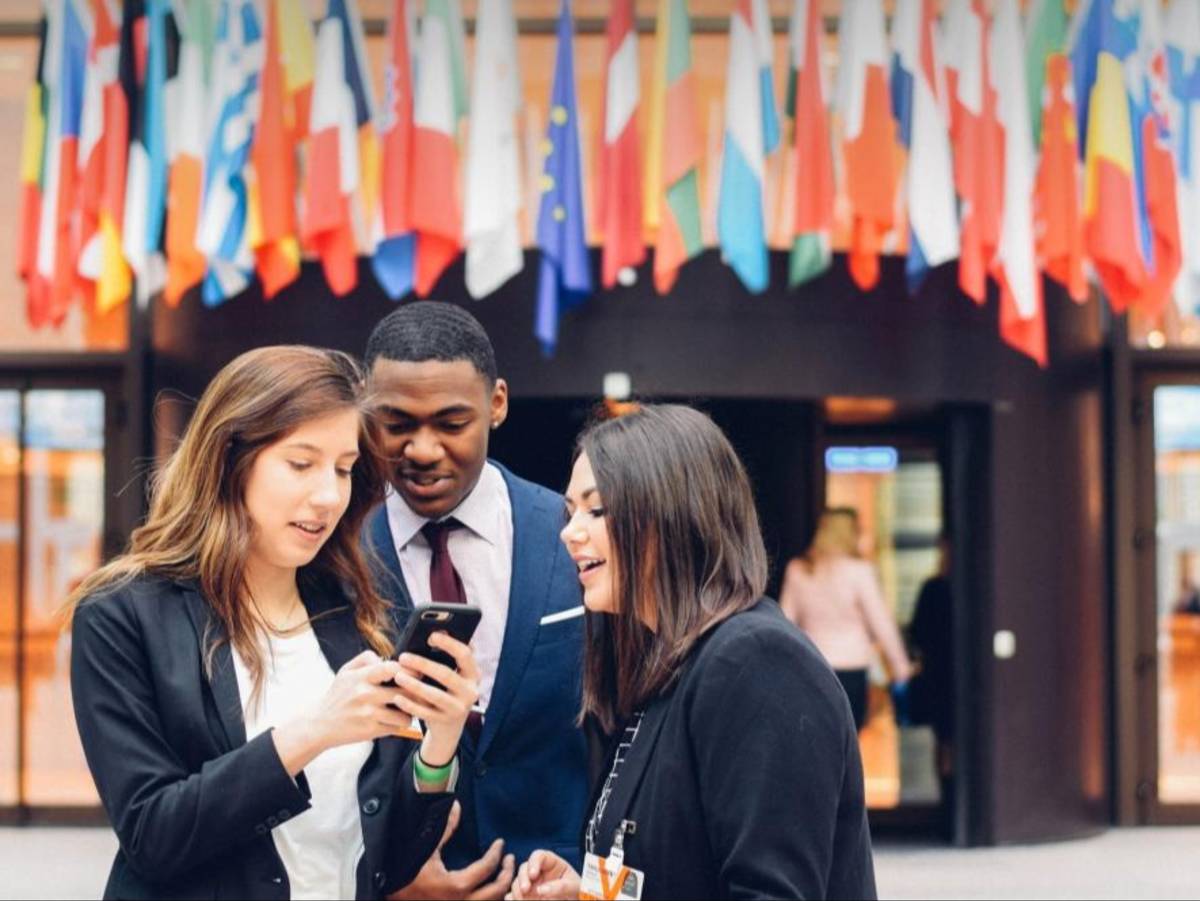 Students look at a phone while dressed in suits outside of the EU headquarters in Brussels, Belgium.