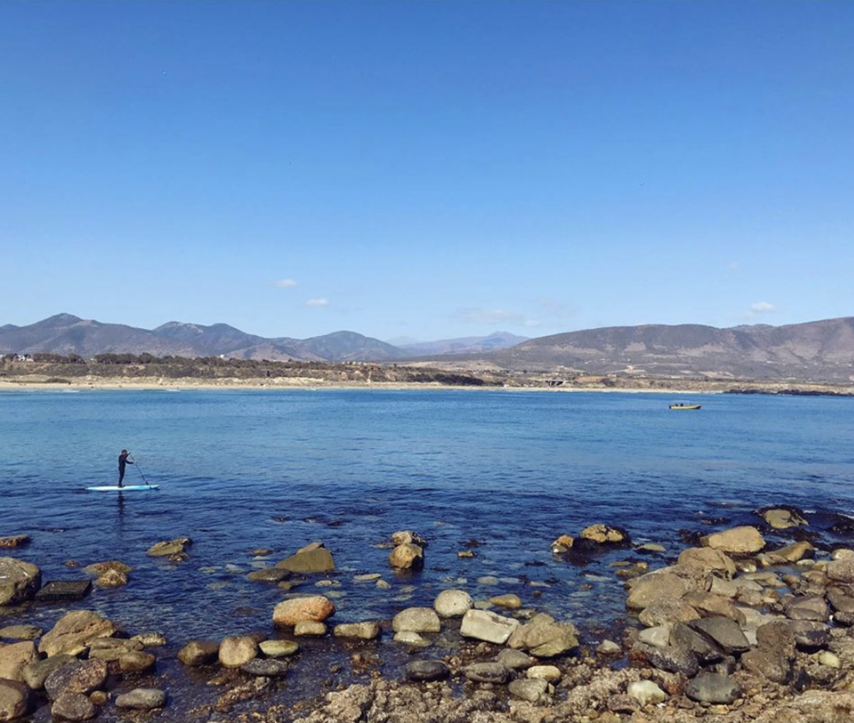 Students paddleboarding on calm Chilean waters during a social work and psychology internship excursion.