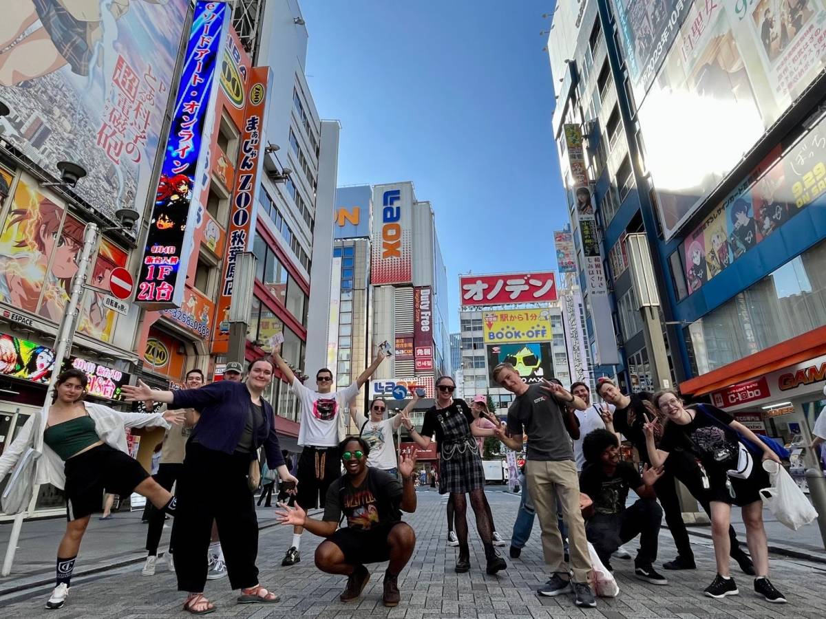 Students posing in the vibrant Akihabara neighborhood with brightly colored signs on tall buildings