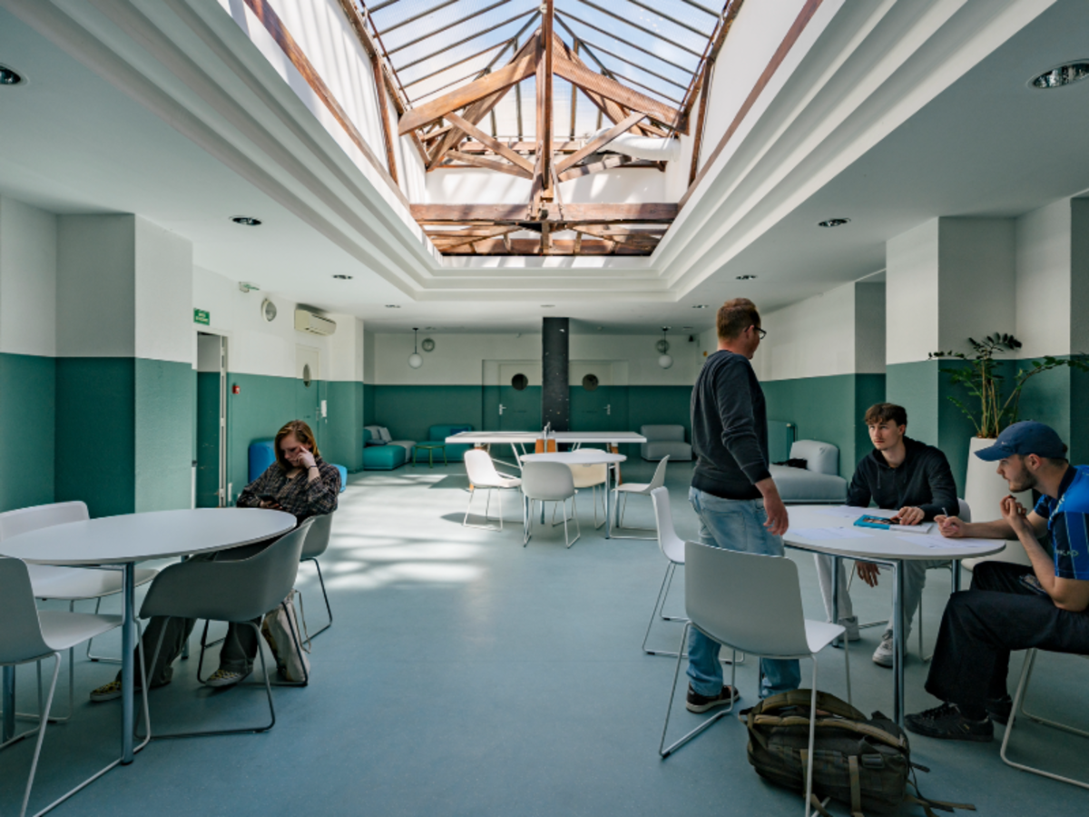 Students relaxing and chatting in a bright common area at EF Nice, with natural light streaming through a glass ceiling.