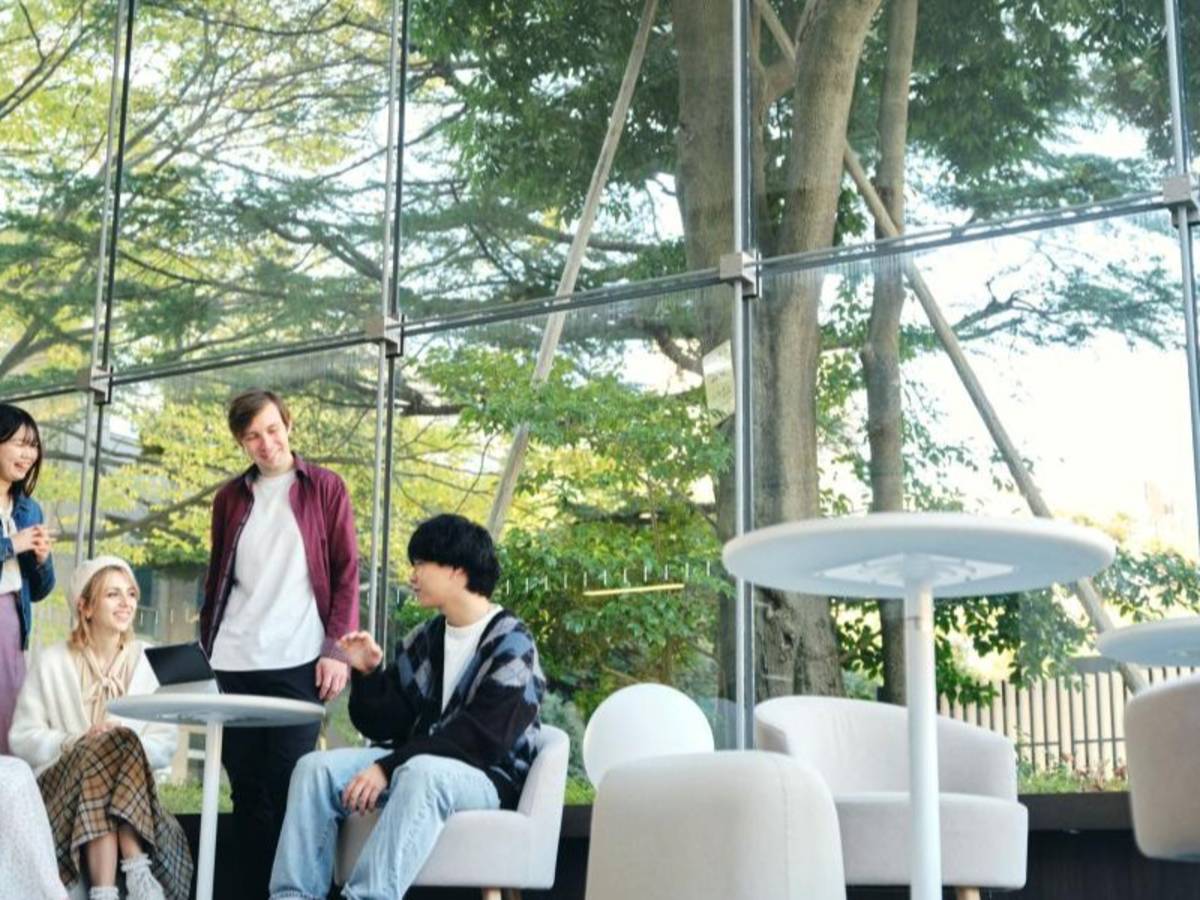 Students sitting and smiling indoors near a window at Musashi University.