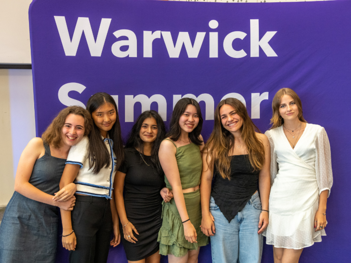 Students smiling next to a Warwick summer sign