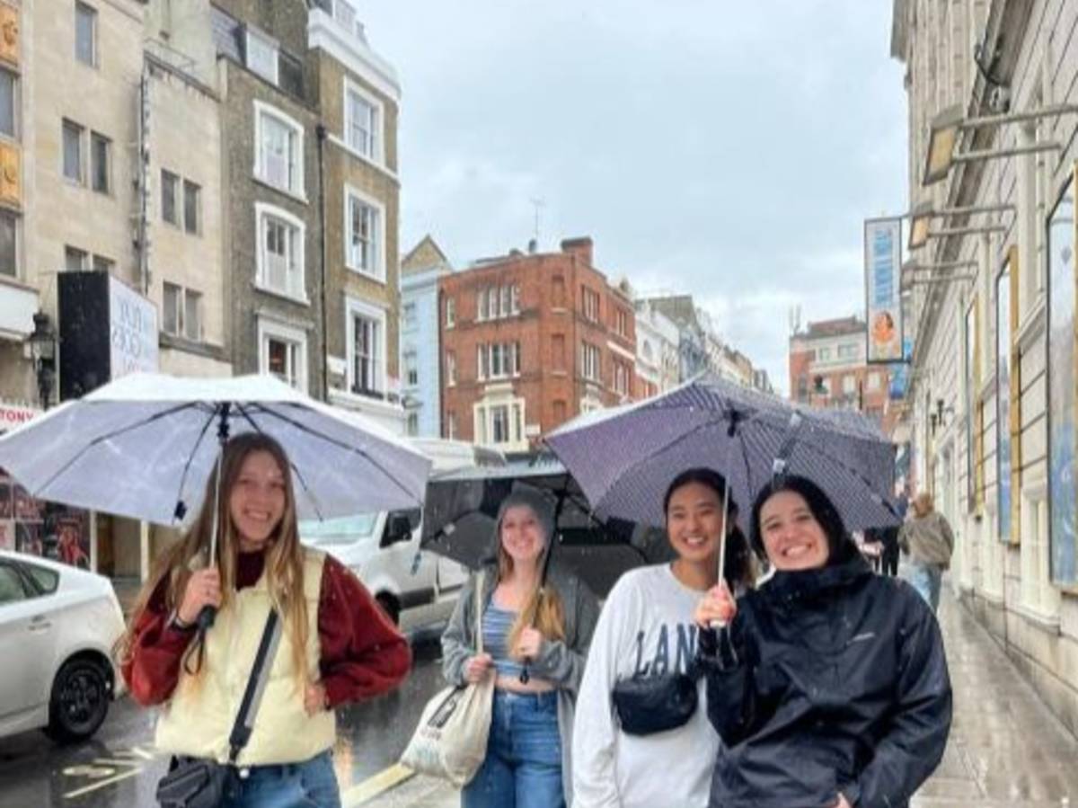 Students walk with umbrellas on a rainy street in London.