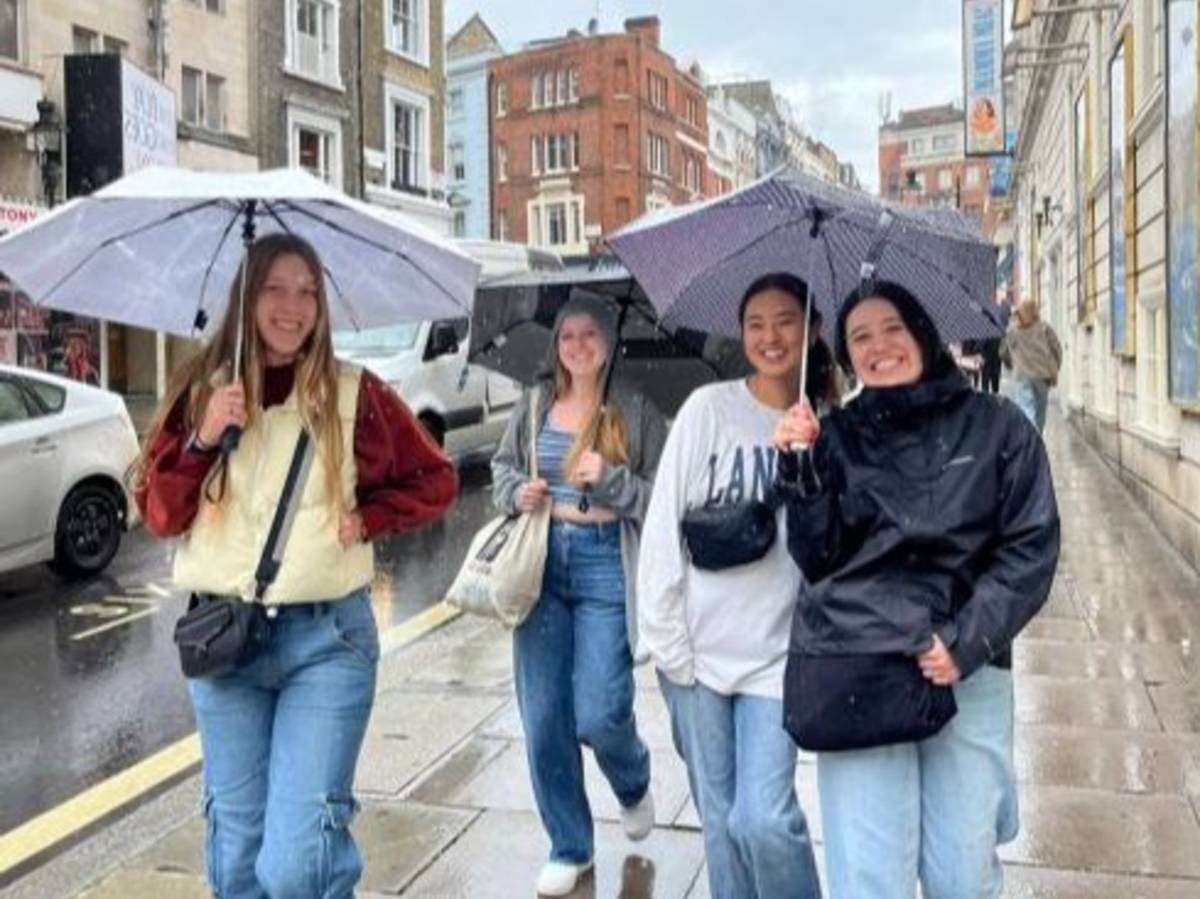 Students walk with umbrellas on a rainy street in London.