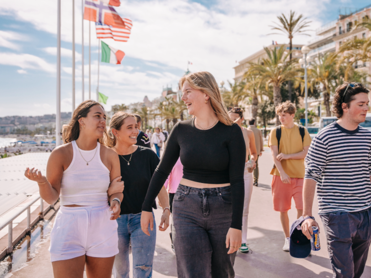 Students walking along the Promenade des Anglais in Nice, enjoying the sunshine, palm trees, and views of the Mediterranean coast.