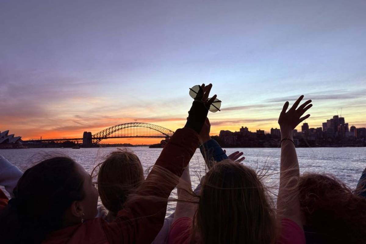 Students waving hands at sunset in front of Sydney Harbour Bridge