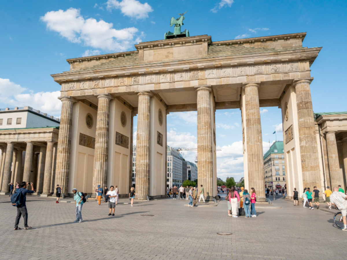 The Brandenburg Gate in Berlin with tourists walking around the historic monument on a sunny day.