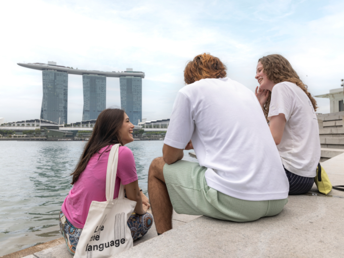 Three EF students sitting by Marina Bay in Singapore, laughing together with Marina Bay Sands in the background.