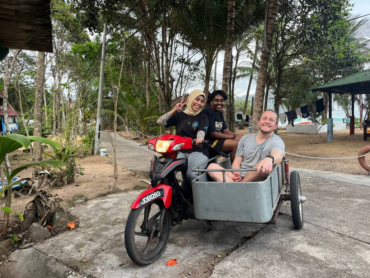 three people riding a red motorcycle with a sidecar