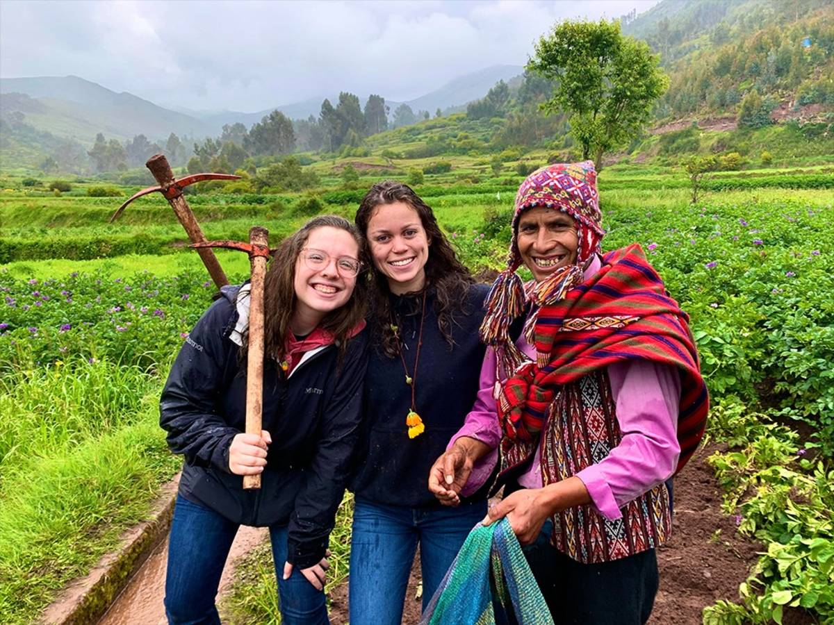 Three people smile together in a lush, terraced field beneath misty mountain.