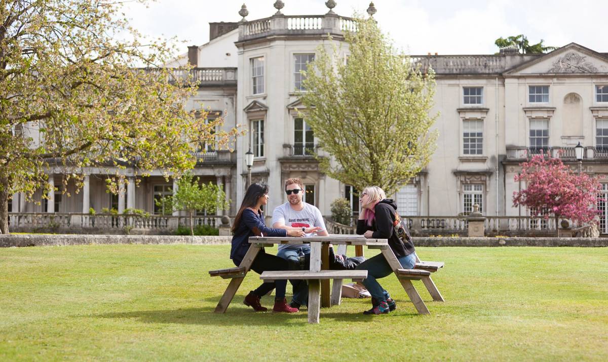 Three students on a bench outside Grove House, University of Roehampton. 