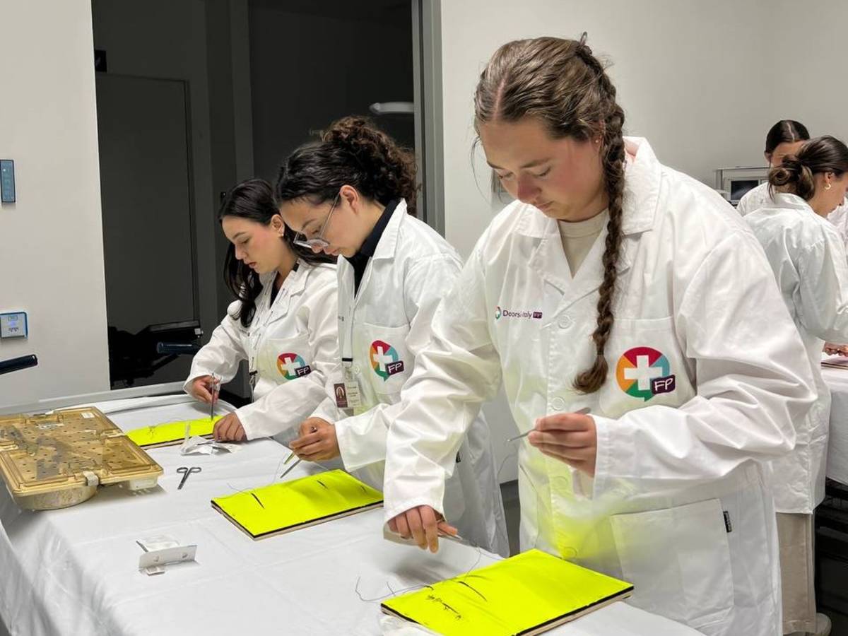 Three students pictured in their program lab coats practicing suture techniques.