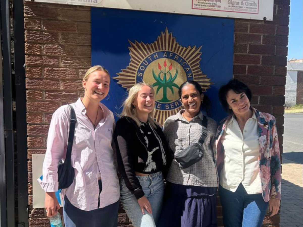 Three volunteers and a member of staff stand in front of a sign for the South African Police Service, smiling  into the camera. 
