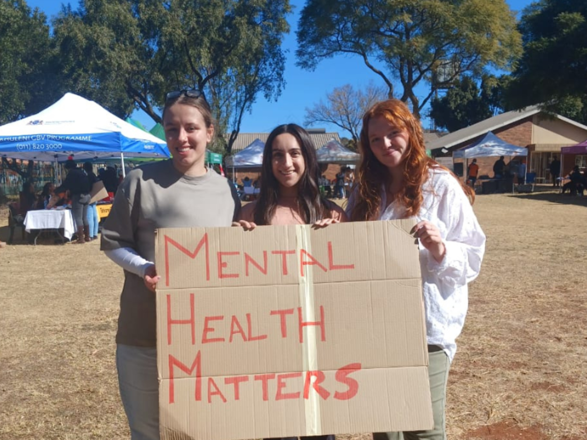 Three volunteers smile as they hold up a cardboard sign that reads 'Mental Health Matters'. 
