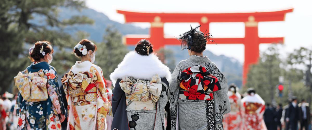 Traditional geisha walk towards a large torii gate