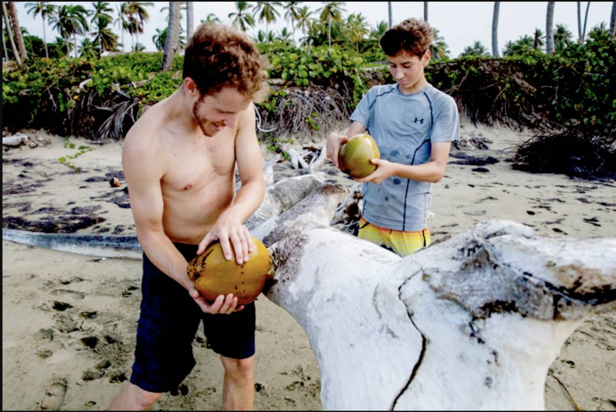 Two boys break coconuts on the beach