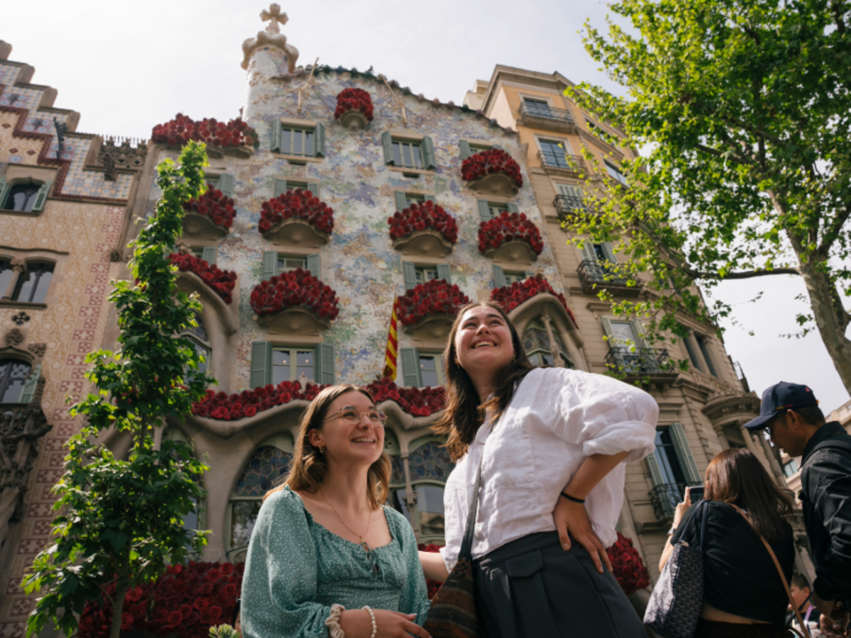 Two EF students smiling in front of Casa Batlló in Barcelona, decorated with red flowers on the balconies.
