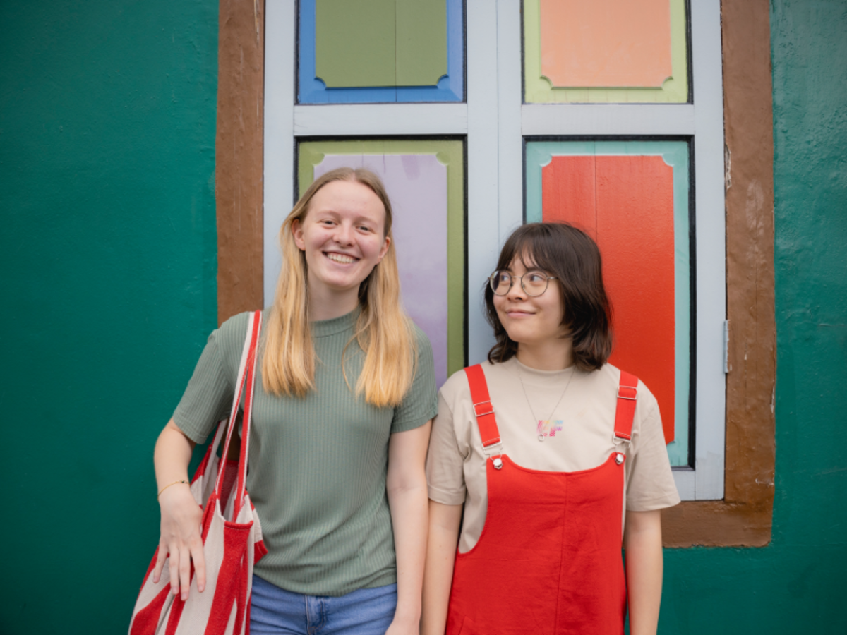 Two EF students standing in front of a colorful painted window in Singapore, smiling and enjoying their study abroad experience.