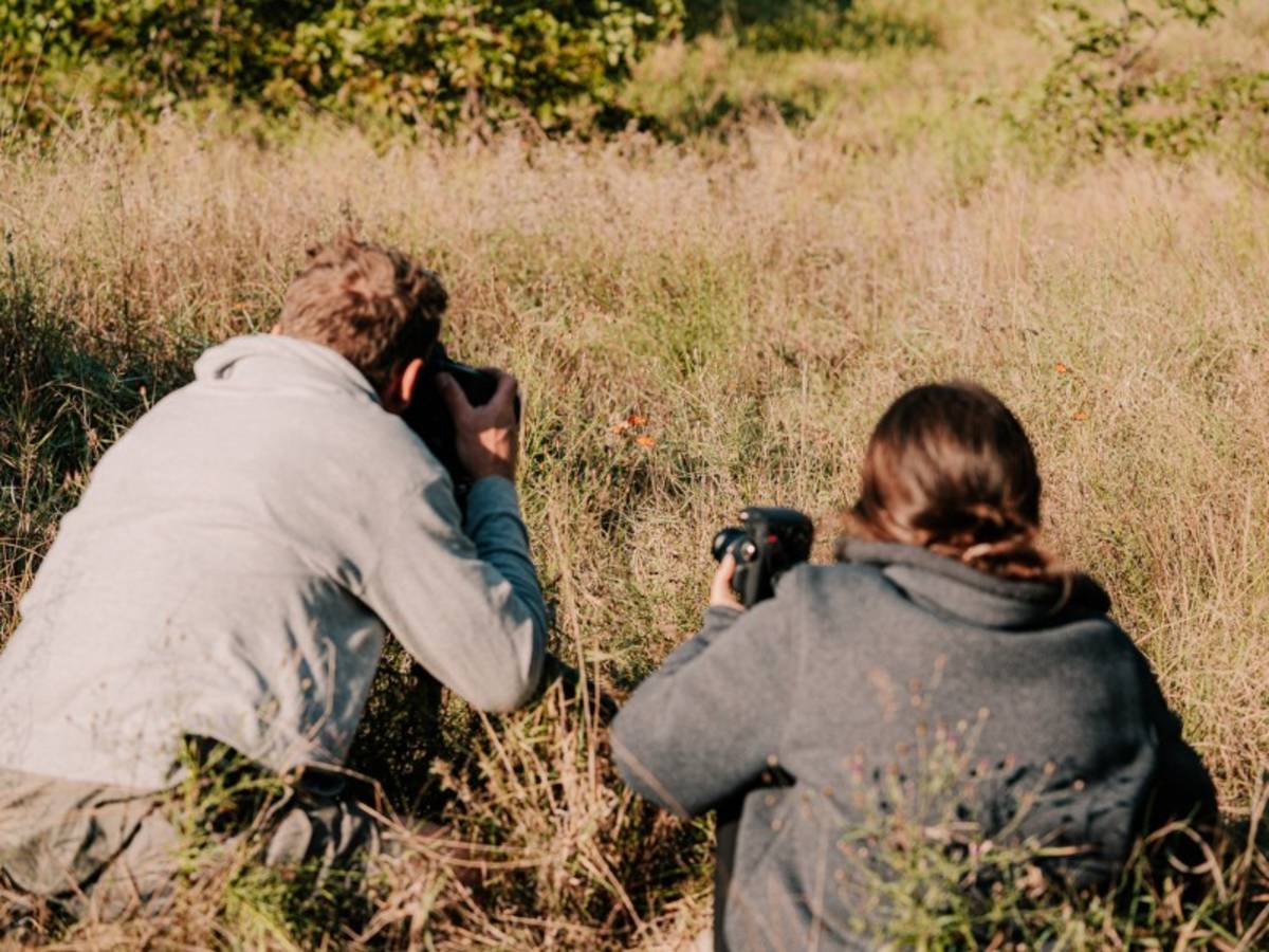 Two guests crouched low photographing wildflowers in tall grass in Kruger on a Penda Photo Tour