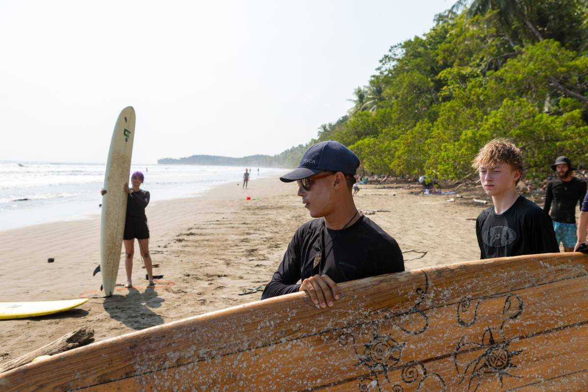 Two people carry surfboard towards ocean