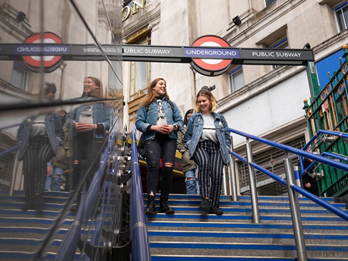 Two students walk down steps with a London Underground sign above them