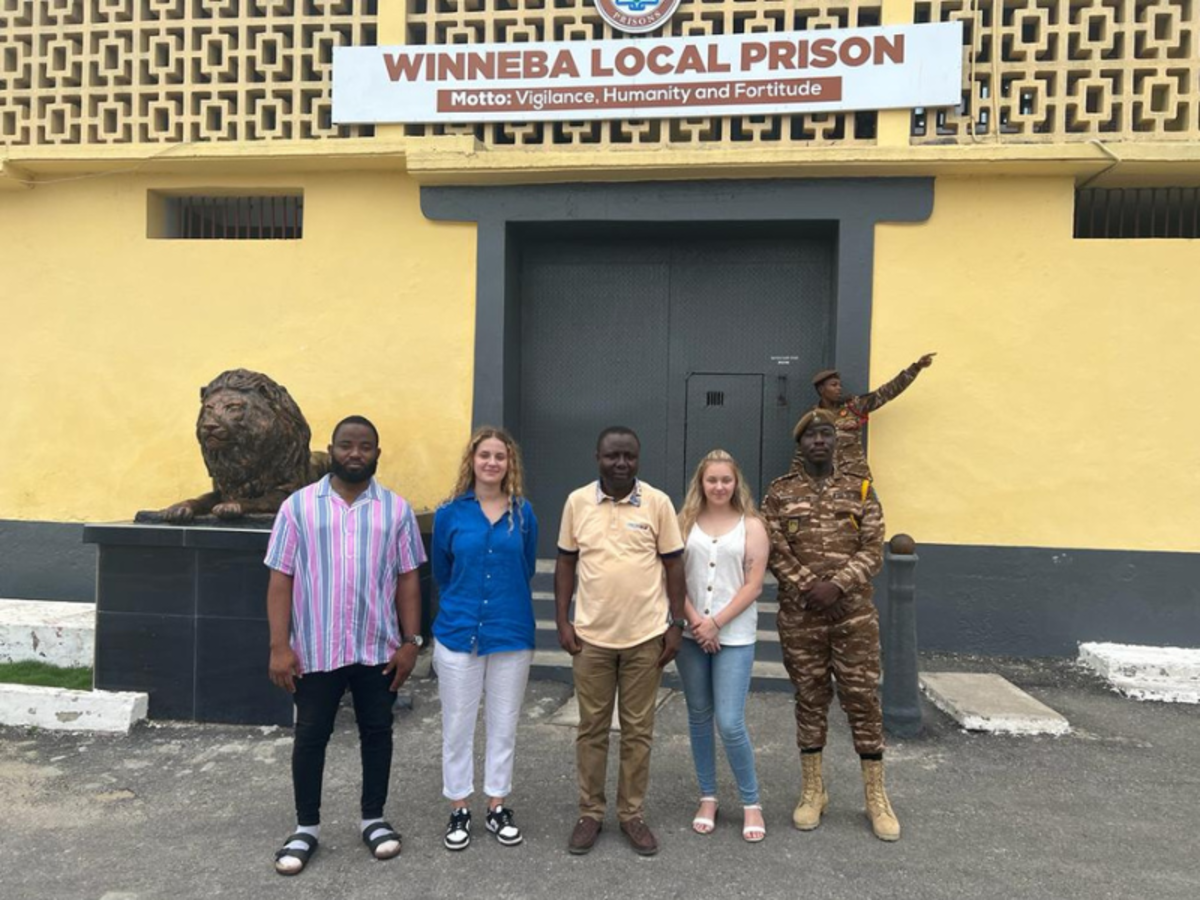 Two volunteers stand with staff and prison officials outside of Winneba Local Prison