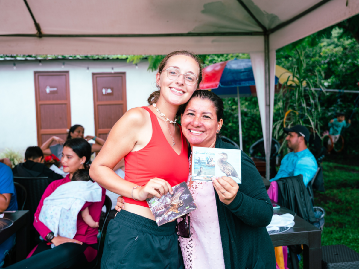 two women pose for a photo while holding postcards
