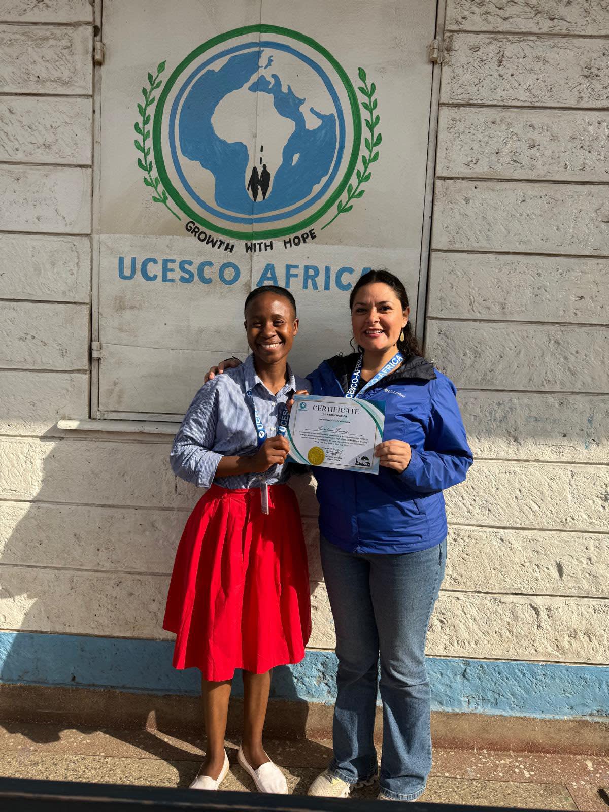UCESCO volunteer holding a certificate, standing beside a local woman