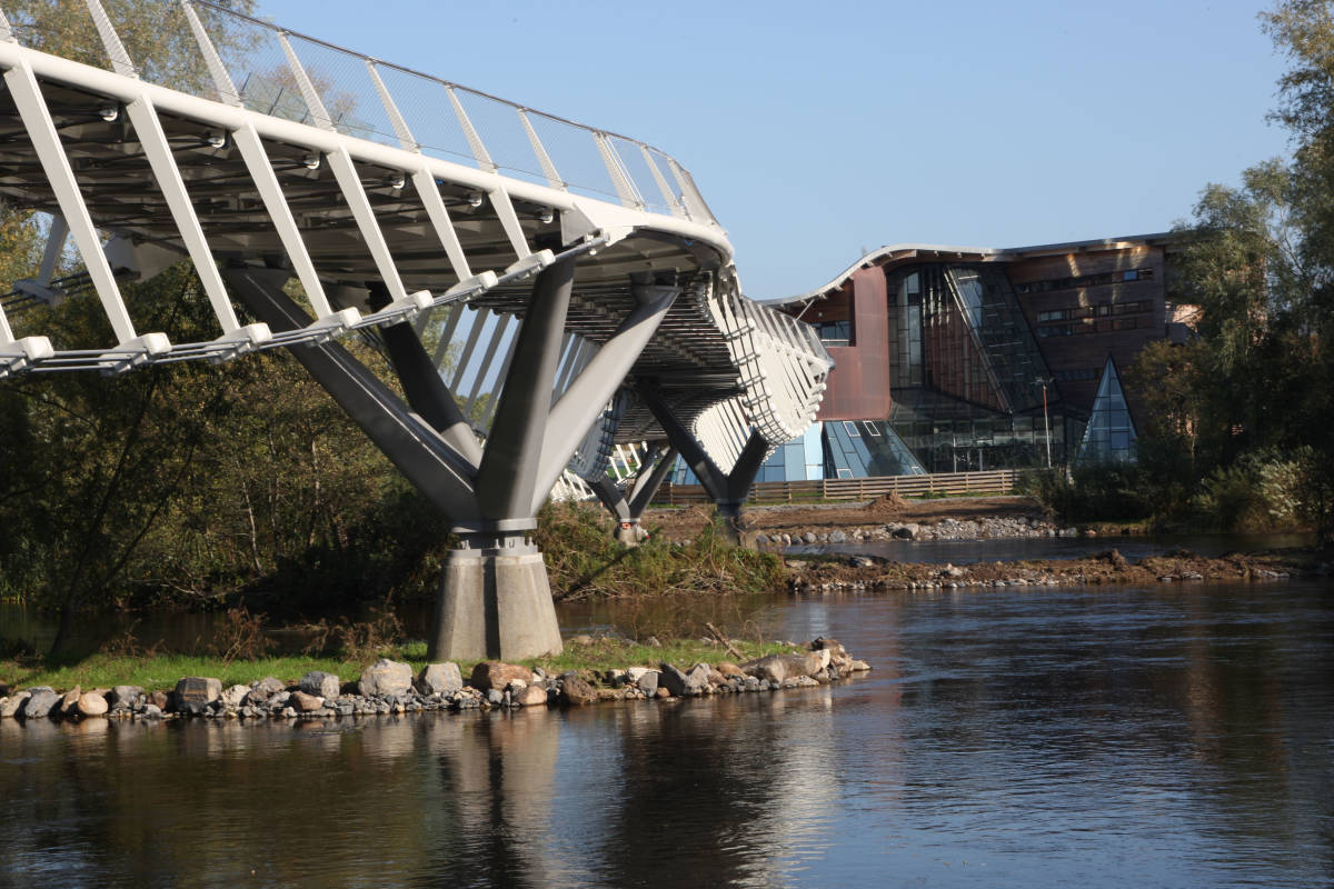 View under a bridge at waters edge looking at a building 