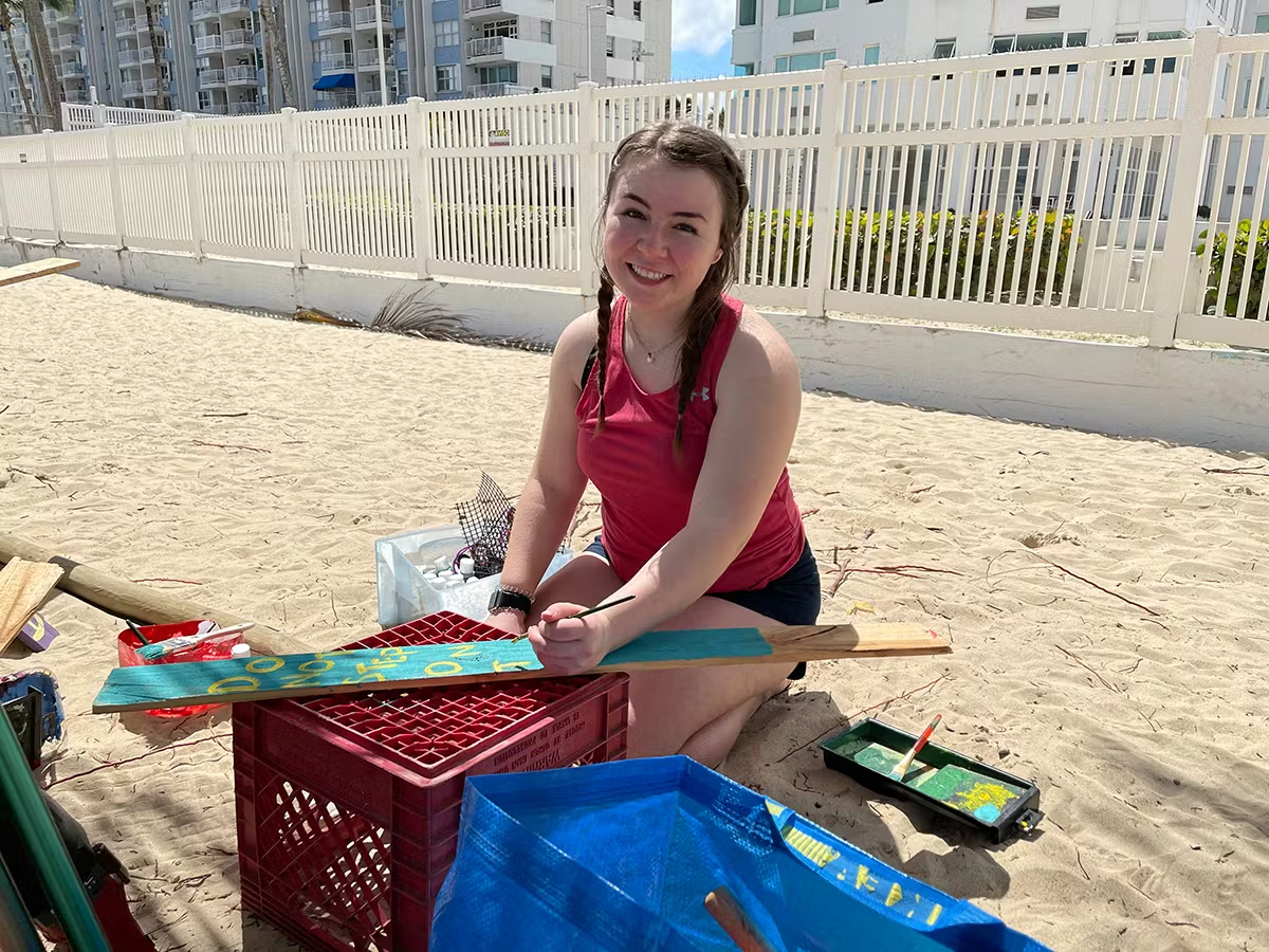 Volunteer painting a wooden sign on the beach