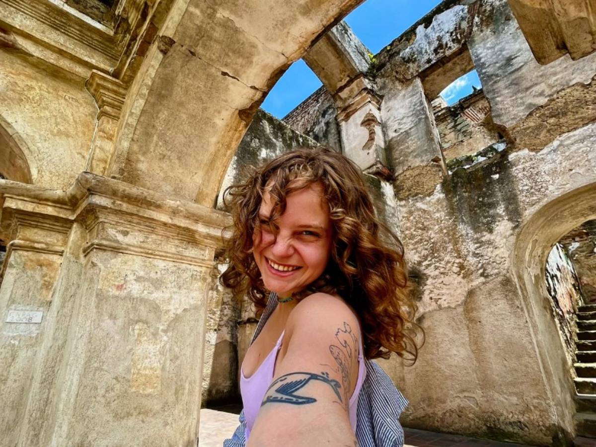 Young woman smiles while taking a selfie in front of crumbling ruins.