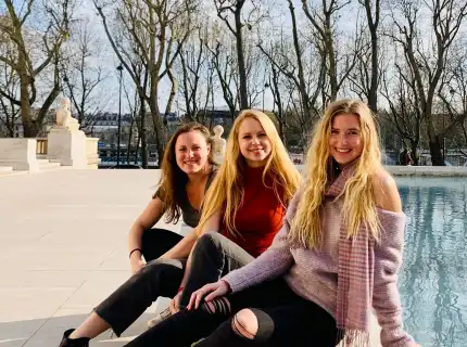 Three women smiling by a pool with Eiffel Tower in the background.