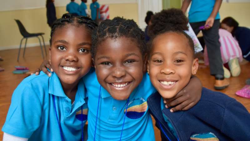 3 primary students in uniforms smiling with arms around each other.