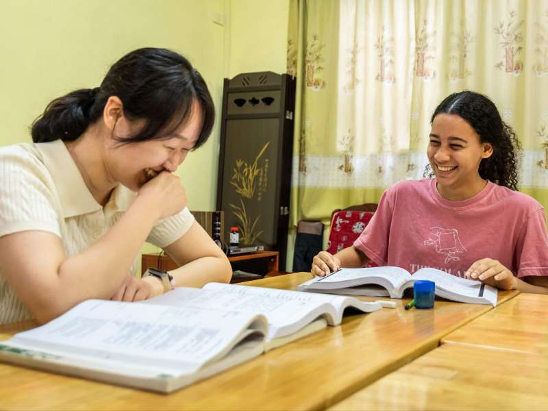 A Chinese teacher and student laugh together over open textbooks during a Mandarin lesson at the CLI Center in Guilin.