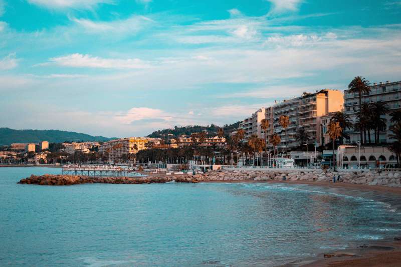 A city with palm trees along a beach with clear blue water and a cloudy blue sky