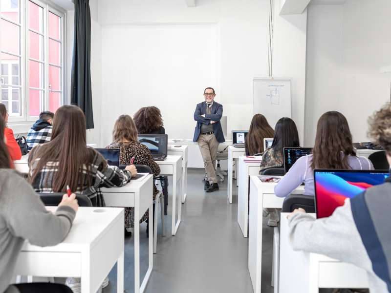 A class of students at their desks facing a smiling teacher