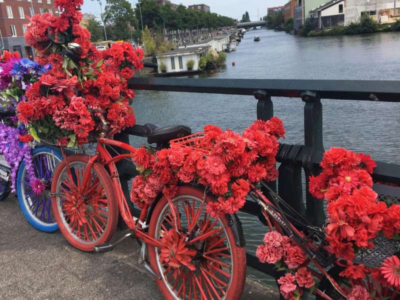A colorful bike full of flowers sits against a bridge in Amsterdam.