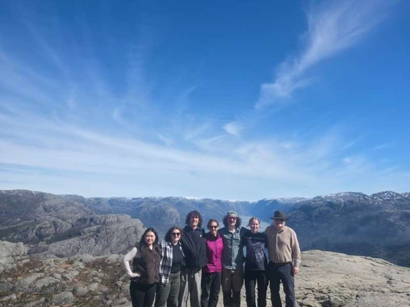 a group of 7 people stand on a mountain with blue skies in the background