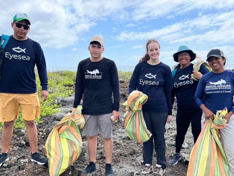 A group of smiling youth with trash bags on the beach.