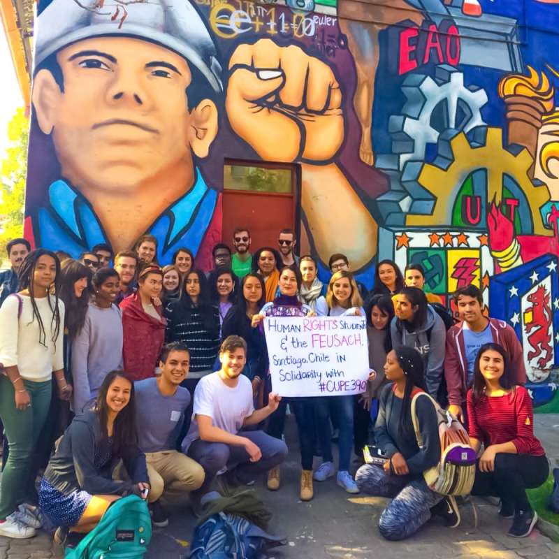 A group of students and Chileans in front of a large mural.