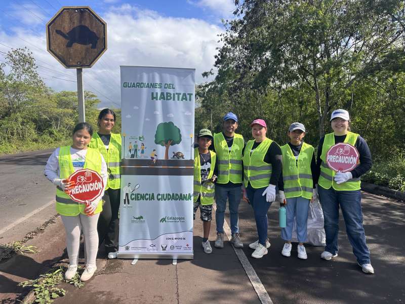 A group poses in traffic vests on road with a banner reading "Guardiants of habitat, citizen science" in Spanish.